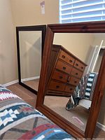 Two large framed mirrors leaning against a wall, showing the brown wood frame with visible grain and black frame.