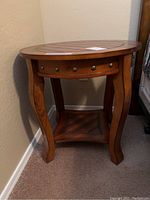 Full view of round wood nightstand showing detailing on top surface, legs, and lower shelf