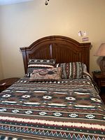 Full view of queen bed with patterned bedding and wooden headboard in good condition
