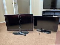 Photo of two Samsung 32-inch TVs side by side on carpet with their remotes lying in front.