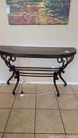 Full view of the entry side table showing the wood grain top with studded sides and black metal curved base with crossbars.