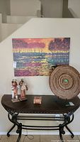 Photo showing all items: unframed canvas wall art of colorful abstract landscape, two paper mache figurines dressed in traditional attire, and a round woven basket on metal stand.