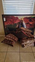 Framed red rock canyon landscape print with waterfall, leaning against a wall with decorative pillows and Southwest blanket arranged on floor.