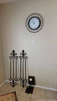 Photo showing two tall cast iron wall sconces on the floor beneath a round metal wall clock on the wall.