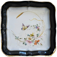 Top-down view of square scalloped porcelain dish decorated with hand-painted butterfly, flowers, and wheat on white interior base with cobalt blue border and gold trim.