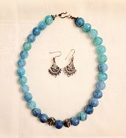 Faceted aquamarine bead necklace laid flat with sterling silver filigree earrings centered inside the necklace circle, highlighting bead size and color gradient.