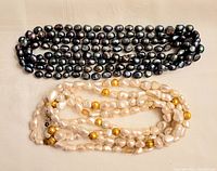 Both grey and cream pearl necklaces laid out on a flat surface, showing full lengths and bead detail.