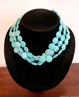 Front view of triple strand turquoise stone necklace on black display bust.