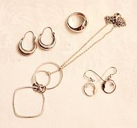 Full view of sterling silver ring, pendant necklace with three linked shapes, crescent-shaped hoop earrings, and round drop earrings.