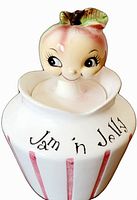 Front view of the white ceramic jam and jelly jar with hand-painted pink vertical stripes, the words 'Jam 'n Jelly' painted in black, and the apple head lid showing a cute smiling face.