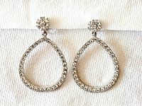 Front view of the crystal hoop clip-on earrings laid on a textured white surface, showing overall shape and crystal arrangement.
