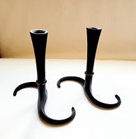 Pair of black cast iron candle holders with curved S-shaped bases standing upright on white surface, showing full front and side view.