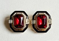 Front view of the pair of vintage ruby crystal clip-on earrings showing the ruby red faceted rectangular crystal centerpiece with black enamel and clear baguette side crystals.
