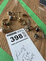 Photo of 10k gold rings with various stones, tie clips, and ASU logo cufflinks displayed on table with MaxSold tag.