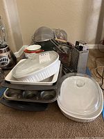 Photo showing stacked glass casserole dishes with lids, metal muffin tins, metal sieves, and kitchen graters along with some measuring cups and small kitchen utensils.