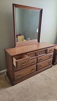 Full view of wood grain dresser with mirror attached. Six drawers with brass handles, decorative front on top central drawer.