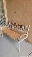 Full front and side view of the outdoor bench showing metal frame, wooden slat seat, and decorative floral backrest.