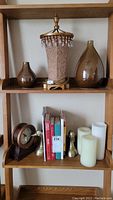 Shelf with decorative lamp, glass vases, clock, books, brass-tone goose bookends, and flameless candles.