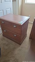 Wood file cabinet from front, showing two closed drawers and silver handles on beige carpet floor.