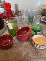 Overall view of glassware lot including bowls, glass tumblers, green textured pitcher, candy dish and stemware.