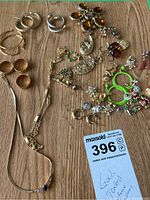 Overview of various gold-toned costume jewelry including earrings, rings, necklace, and brooch laid out on wooden surface.