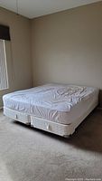 Photo displaying mattress and box spring with white fitted sheet on bed frame in corner of room.