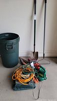 Full lot visible including trash bin, rake, shovel, electric garden tools, and extension cords.