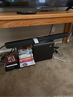 Polk sound bar and subwoofer with stacked DVDs beneath table beside a television, showing the full set included in the lot.