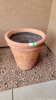 Image of a large terracotta outdoor plant pot on gravel ground near stucco wall.