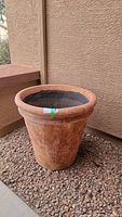 Full side view of large terracotta planter pot sitting on gravel against adobe wall, showing wide flared rim and tapered cylindrical body.