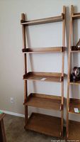 Full front view of the entire solid wood leaning bookcase with five shelves against a wall.