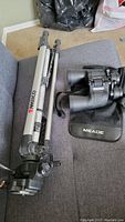 Meade binoculars next to Ambico tripod on fabric surface
