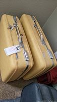 Two yellow toned vintage American Tourister suitcases with keys resting on top, showing metal latches and handles.