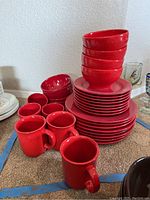 Stack of red dinner plates, smaller plates, bowls, and coffee mugs in red ceramic.