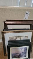 Photo of stacked framed prints against wall showing wood grain and black frames with tissue paper inside some frames