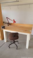 Front angle view of the workbench with vice grip on left side, red clip-on lamp attached, and brown office chair positioned in front.