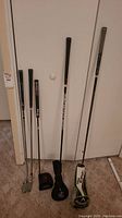 Five golf clubs propped against a door showing full length of shafts and head covers