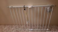 White metal pet gate leaning against wall with tags and packaging attached.