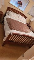 Full view of queen bed with wooden slatted headboard and footboard, warm cherry finish, bedding included for scale
