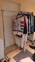 Full view of the chrome steel clothing rack loaded with various garments on hangers, showing rolling caster wheels and structure.