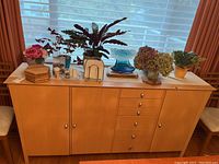 Front view of the light brown wood cabinet showing all drawers and doors with decorative items on top.