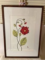 Framed flower art print showing the full image including large red flower, green leaves, and artist's initials in bottom right corner.