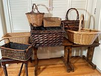 Seven assorted woven baskets arranged on and around a dark wooden table against a louvered background.