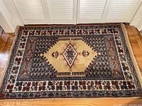 Full view of rectangular wool carpet with central diamond medallion and floral border on wooden floor.