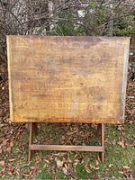 Front view of vintage wooden drafting table showing work surface with wear marks and stains.