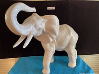 Front and side view of large white ceramic elephant figurine against a dark background.