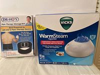 Photo showing both boxed items: Dr. Ho Pain Therapy Massage Belt and Vicks WarmSteam Vaporizer.