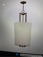 Full view of the bronze hanging light with white cylindrical shade suspended by a chain, displayed against a white background.