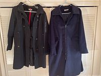 Two ladies coats hanging: Jones New York black coat with hood and Brian Bailey navy blue felt coat.