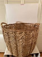Front angled view of large woven basket showing braided handle, zigzag woven pattern and natural fiber construction.
